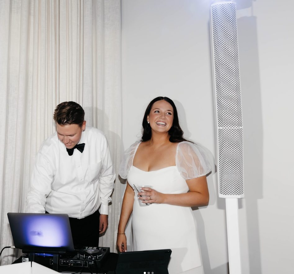 Jackson in a bow tie at a DJ laptop beside a smiling bride